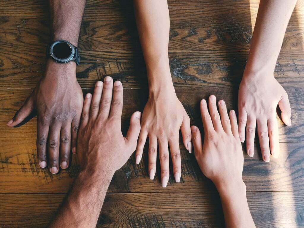 Cinco mãos humanas em uma superfície de madeira.